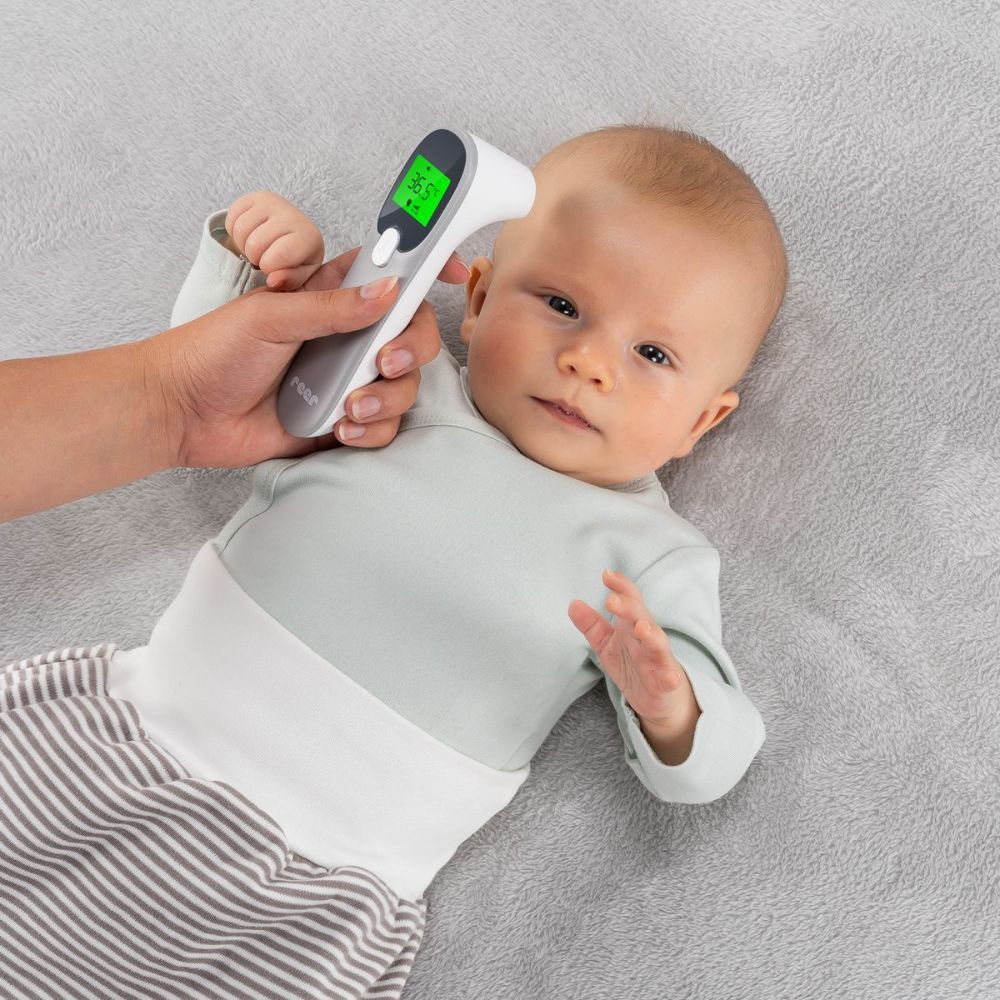 Personne mesure la température d'un bébé avec un thermomètre infrarouge. Le thermomètre affiche 36,5°C. Marque : reer.