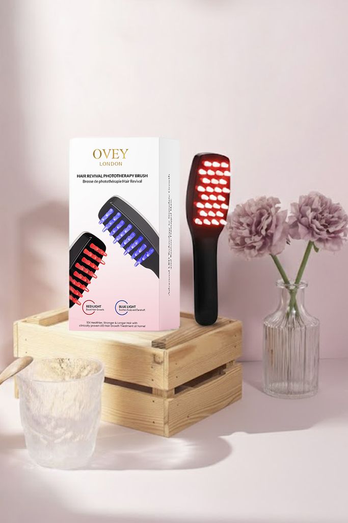 Brosse à cheveux avec lumière rouge et emballage. Emballage avec image du produit et texte. Placé sur un socle en bois.