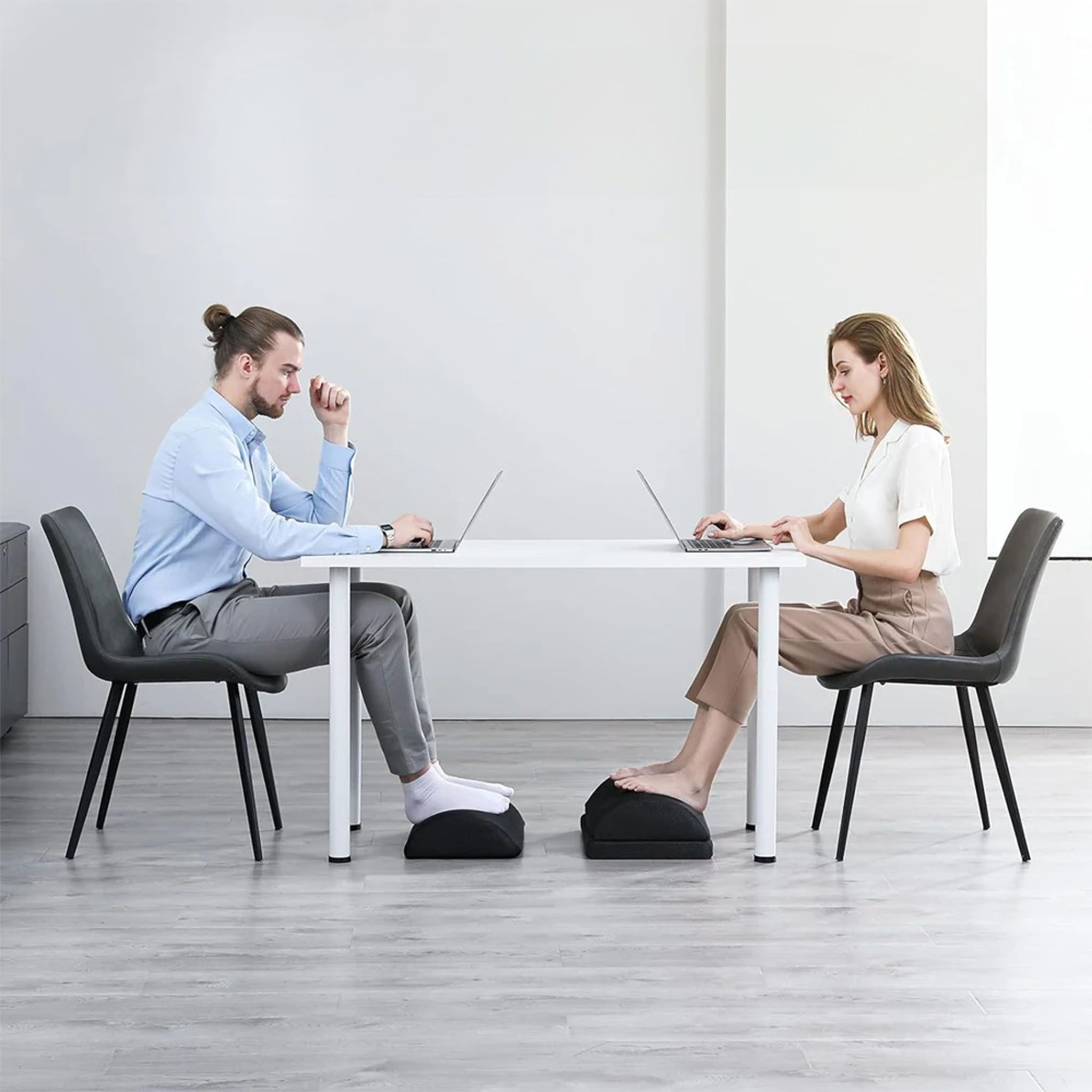 Twee personen werken op laptops aan een bureau. Beiden hebben een zwarte voetensteun.