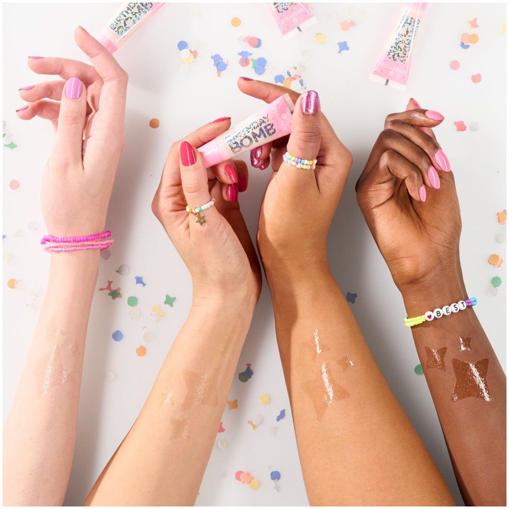 Trois mains tenant des tubes de gloss. Inscription BIRTHDAY BOMB. Différents tons de peau, confettis en arrière-plan.
