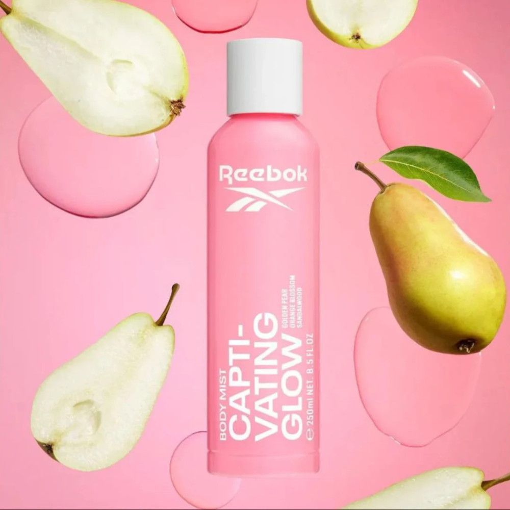Flacon de brume corporelle rose avec bouchon blanc. Logo Reebok et texte 'Captivating Glow'. Entouré de poires et de gouttes roses.