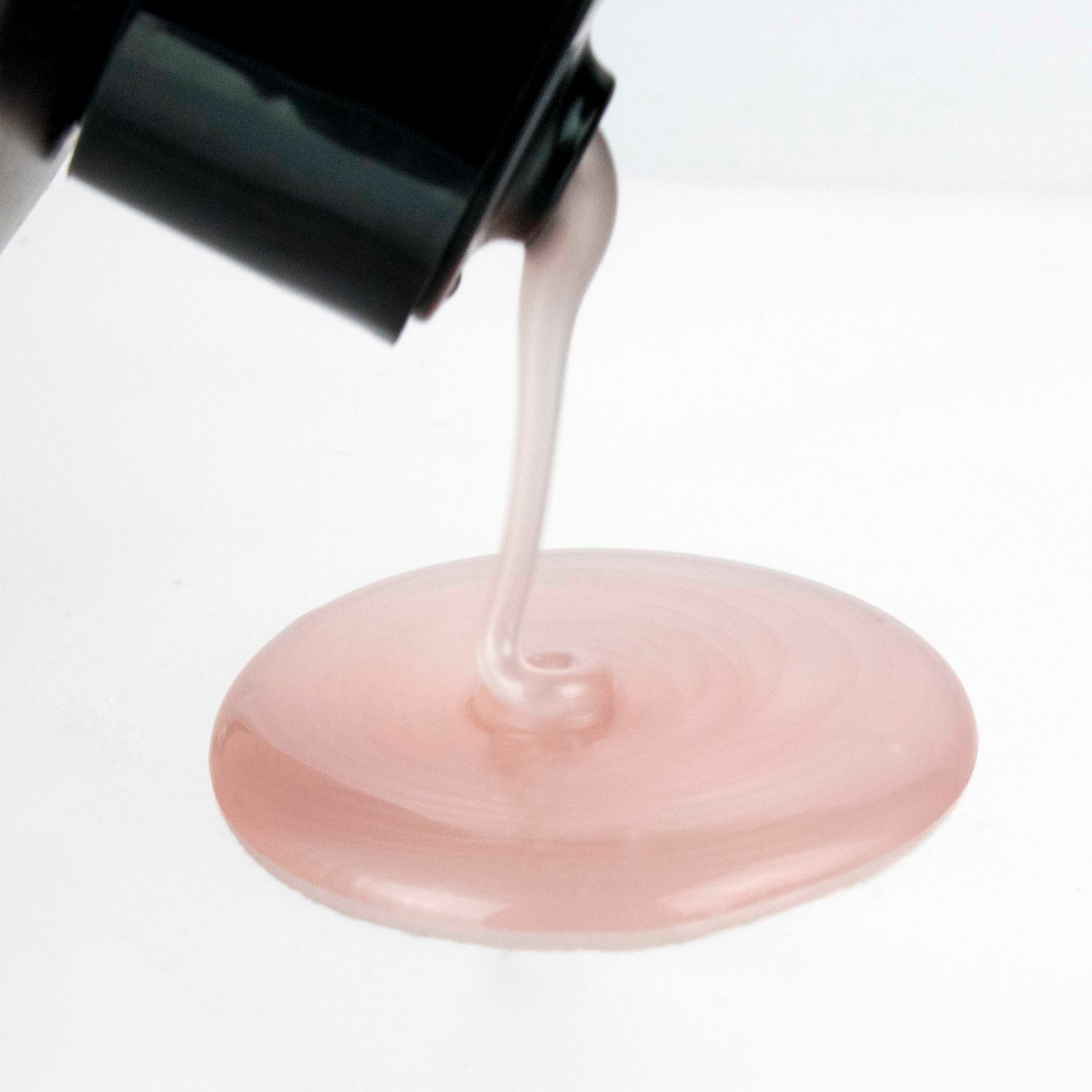 Roze shampoo die uit een zwarte fles stroomt. De achtergrond is wit. De vloeistof vormt een klein meer.