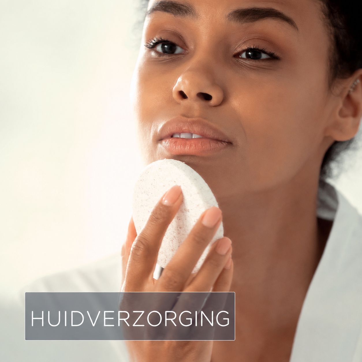 Een vrouw gebruikt een witte, ronde spons voor huidverzorging.