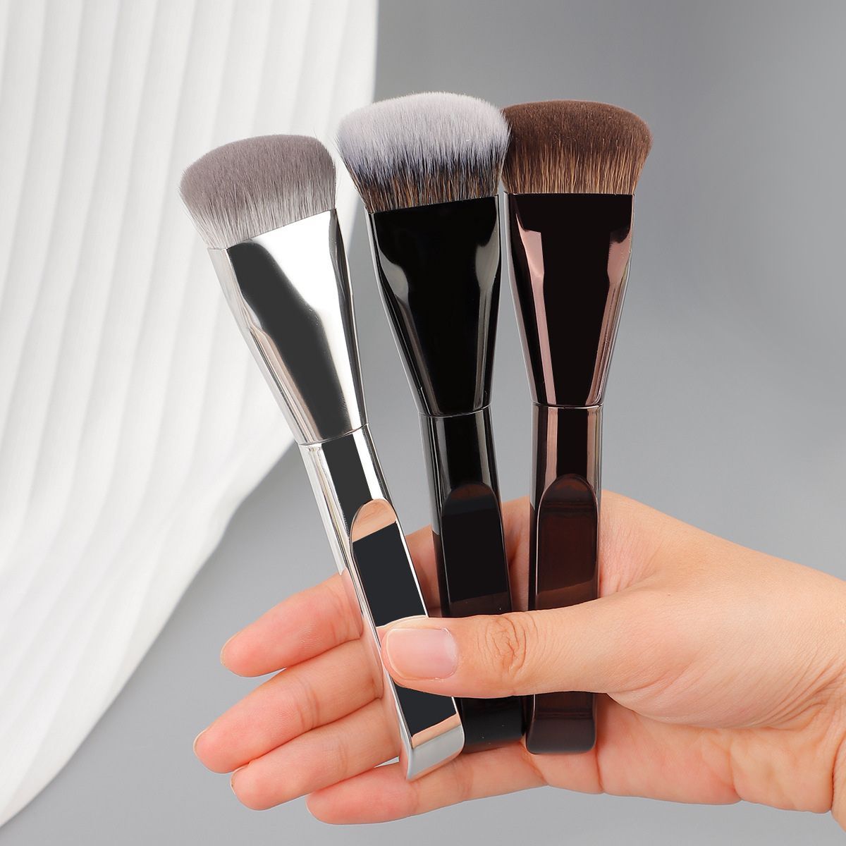 Trois pinceaux de maquillage plats avec manches argenté, noir et marron.