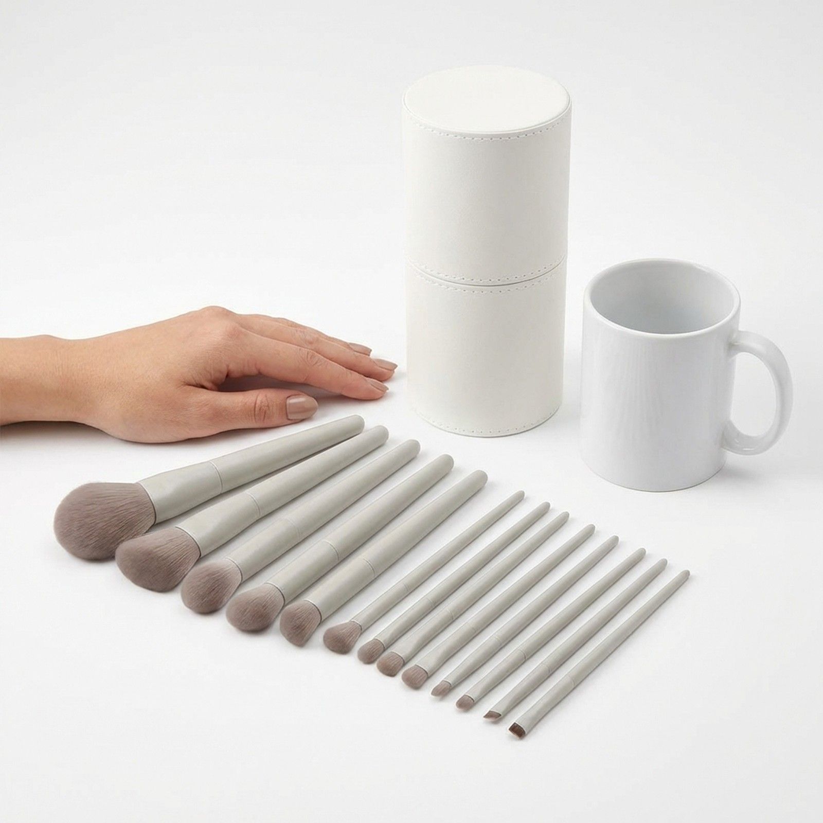 Un ensemble de 12 pinceaux de maquillage gris clair avec manche blanc et une boîte de rangement ronde blanche.