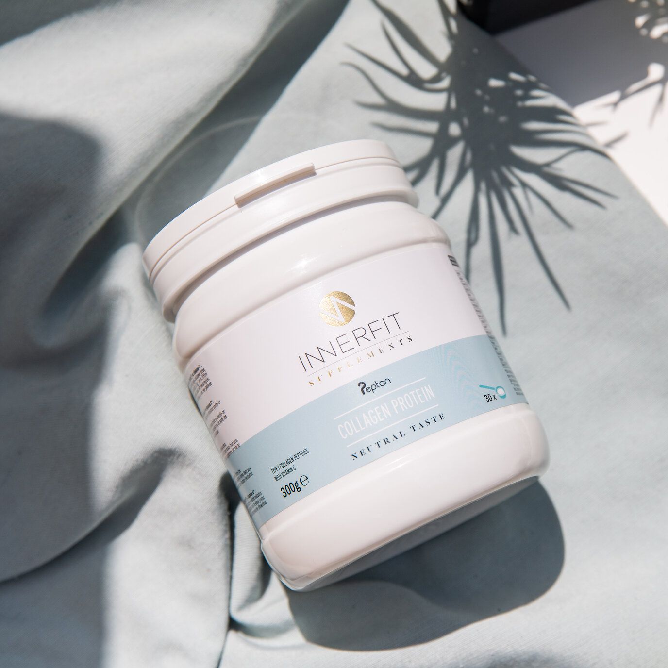Pot blanc "Innerfit" avec logo et texte "Collagen Protein". Inscription "Neutral Taste". Posé sur tissu bleu.
