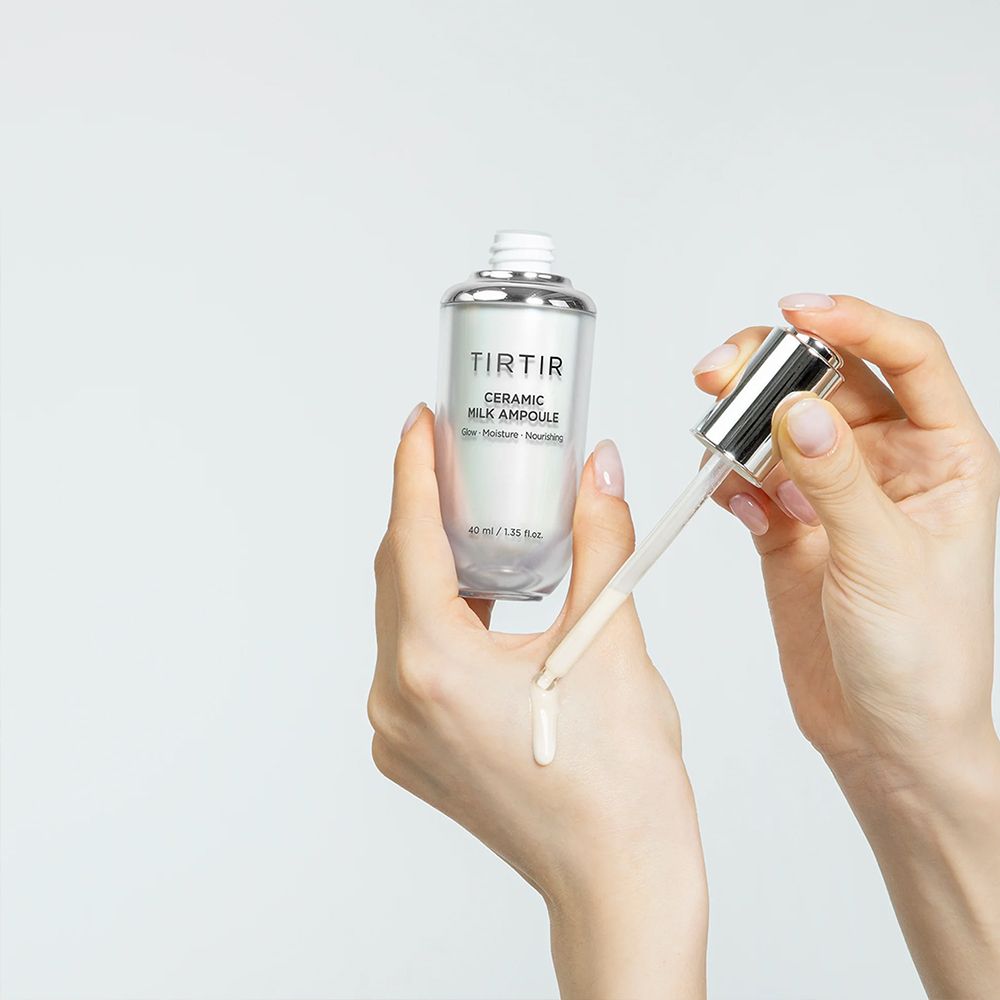Handen brengen TIRTIR Ceramic Milk Ampoule aan, met druppels op de huid.
