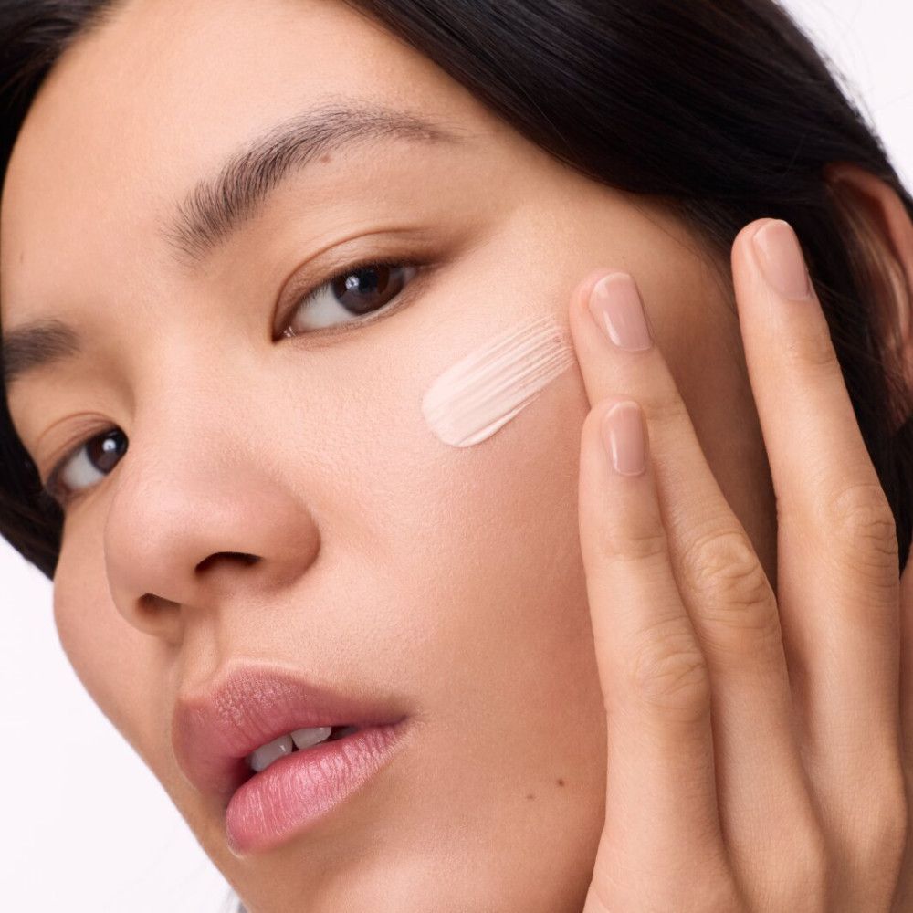 Vrouw brengt primer aan. Gezicht van een vrouw die primer op haar wang aanbrengt. Huidtint primer aangebracht met vinger.