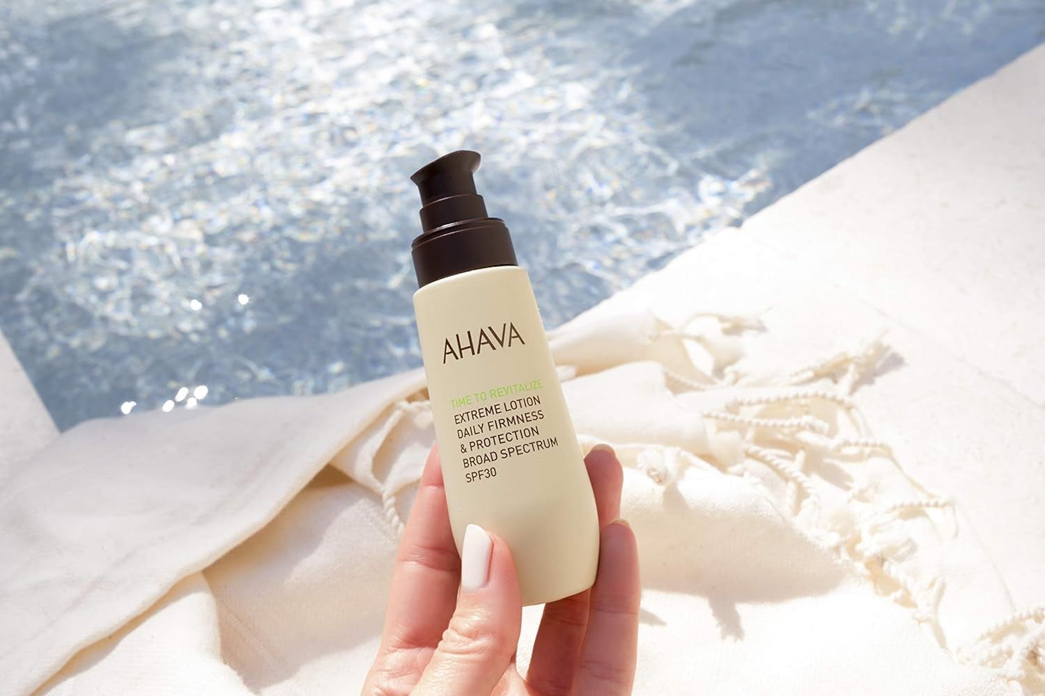 Ahava T.T.R. Extreme Lotion SPF30 in een hand bij een zwembad.
