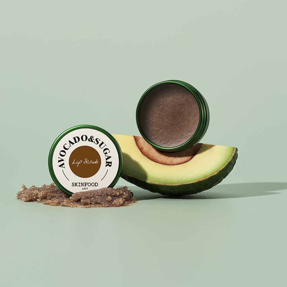 Twee groene potten, één open, naast een avocado en lip scrub. Opschrift: AVOCADO & SUGAR, SKINFOOD.