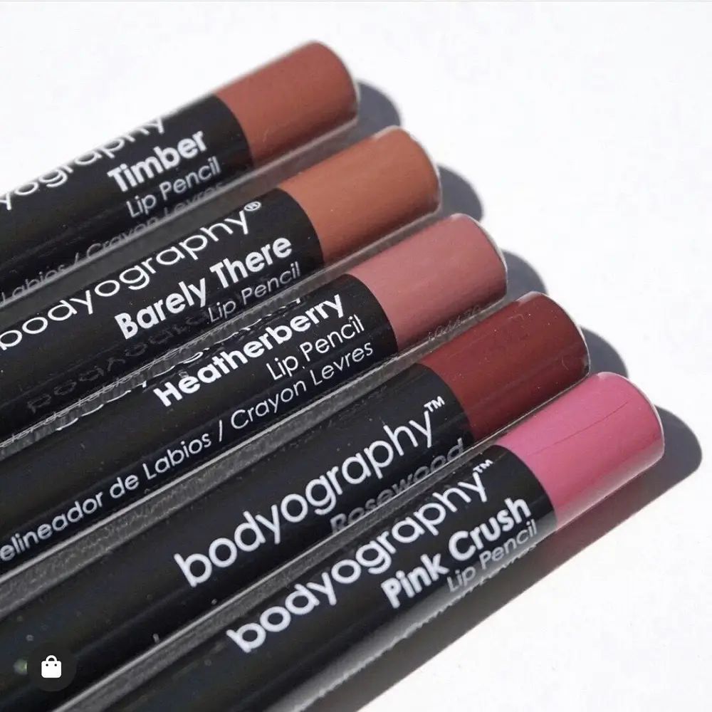 Vijf lippenstiften naast elkaar. Zwarte schachten met productnamen. Kleuren: Timber, Barely There, Heatherberry, Rosewood, Pink Crush. Opschrift: BODYOGRAPHY.