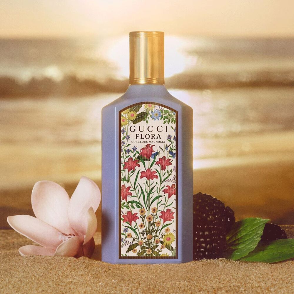 Flacon Gucci Flora Gorgeous Magnolia avec étiquette florale. Bouchon doré. Fond de plage.