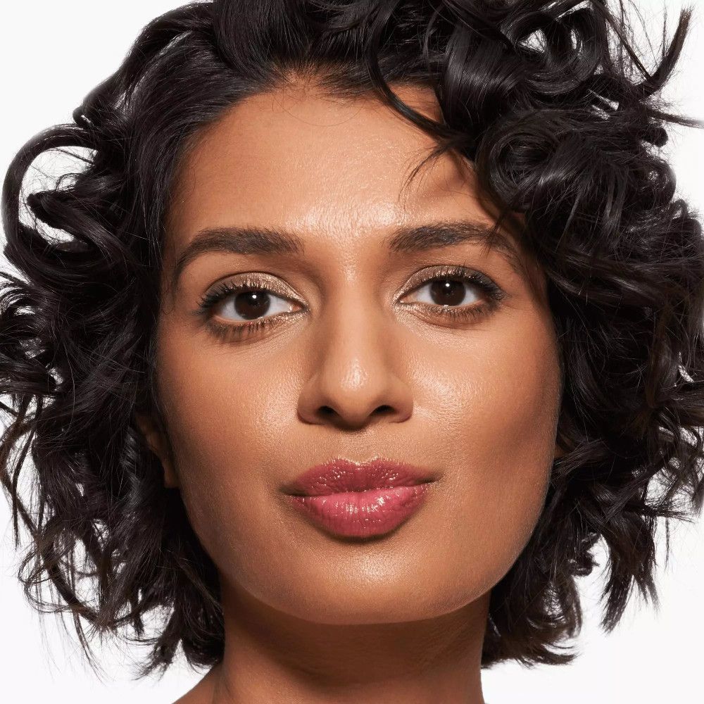 Portrait d'une femme portant du baume à lèvres. Peau foncée, cheveux bouclés, lèvres roses.