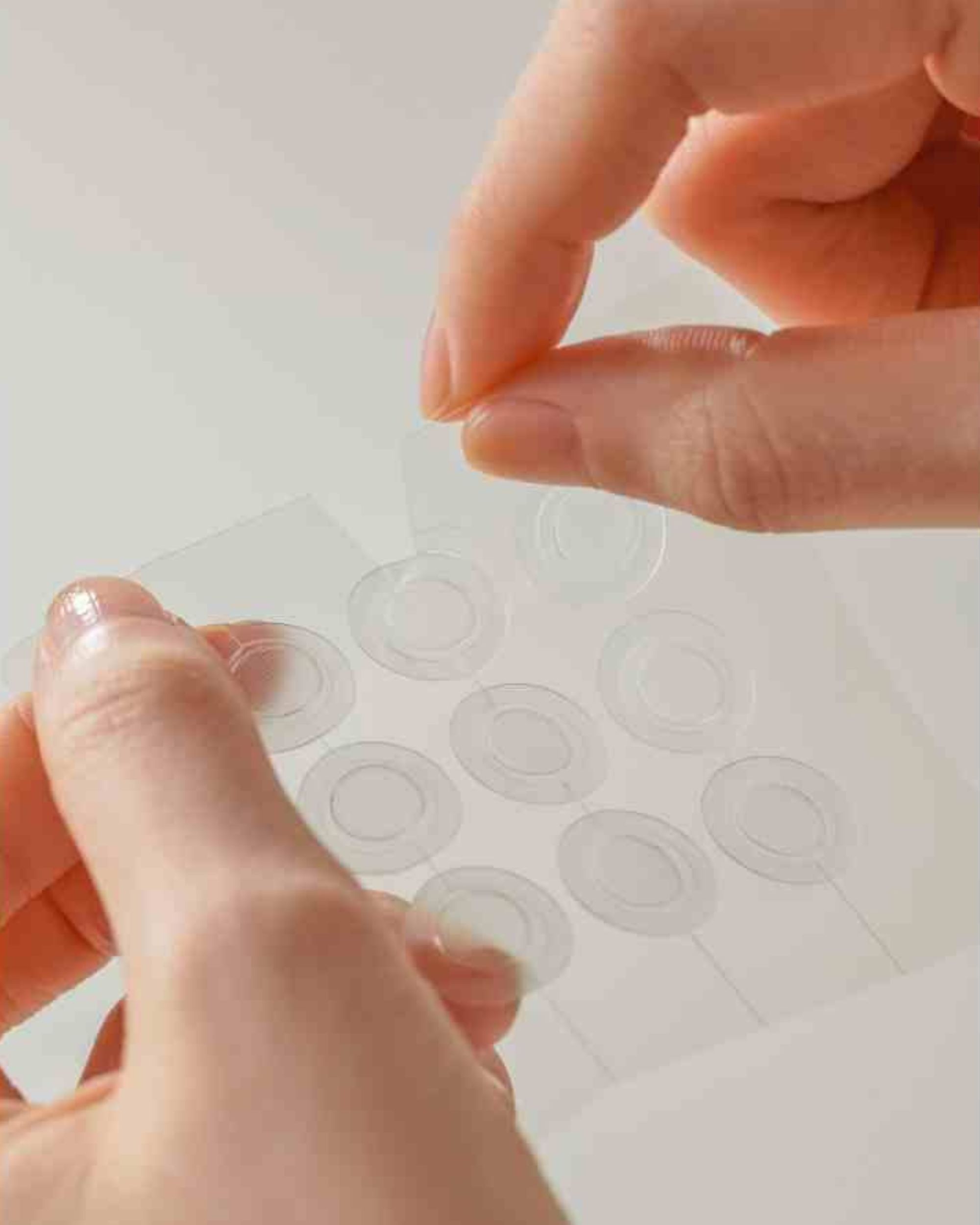 Handen verwijderen transparante, ronde patches van een transparante folie. 10 patches zichtbaar.
