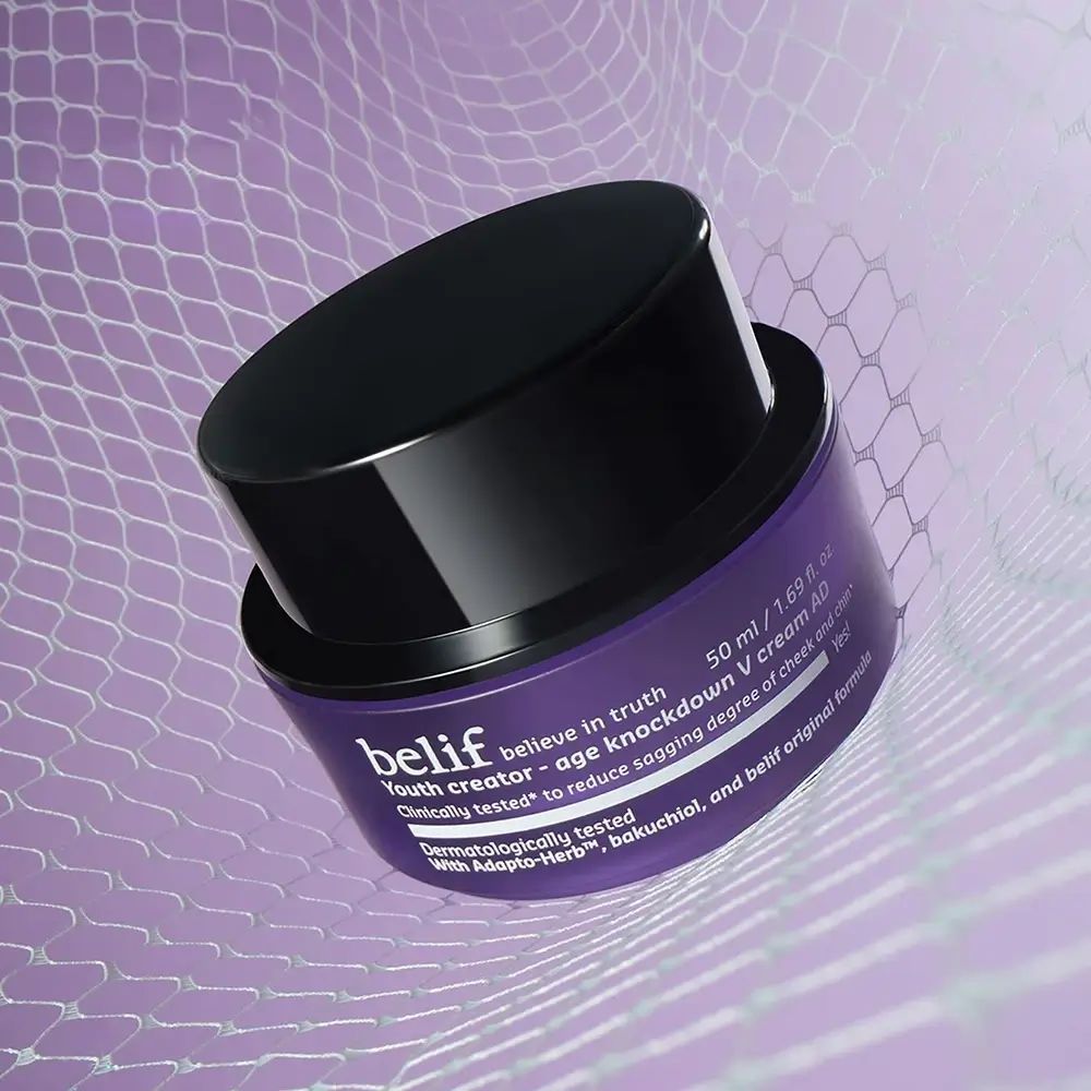 Paarse pot met zwarte deksel, licht geopend. Opschrift: belif, Youth creator - age knockdown V cream AD. Tekst: Klinisch getest, met Adapt-Herb.
