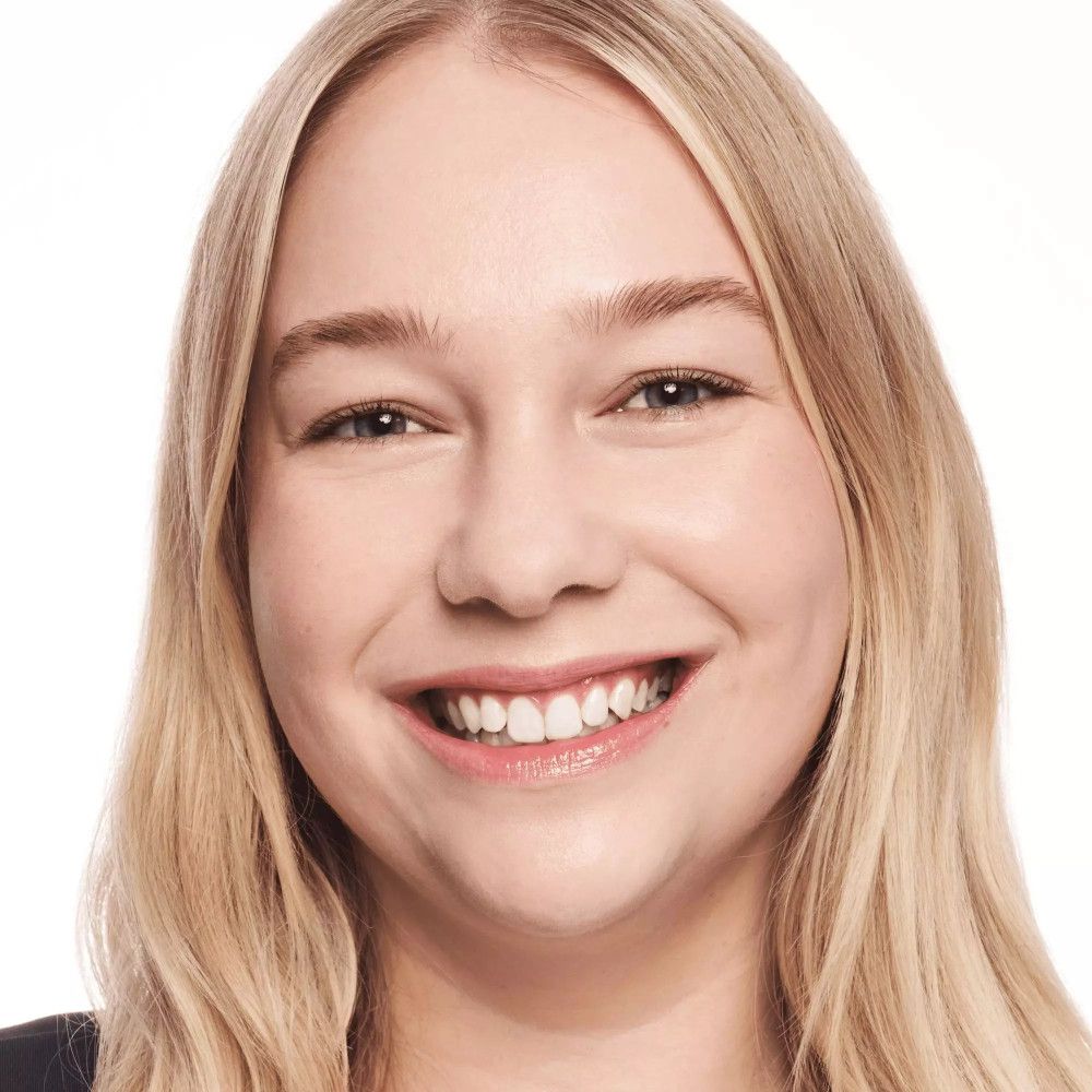 Portrait d'une femme aux cheveux blonds et au visage maquillé. Elle sourit.