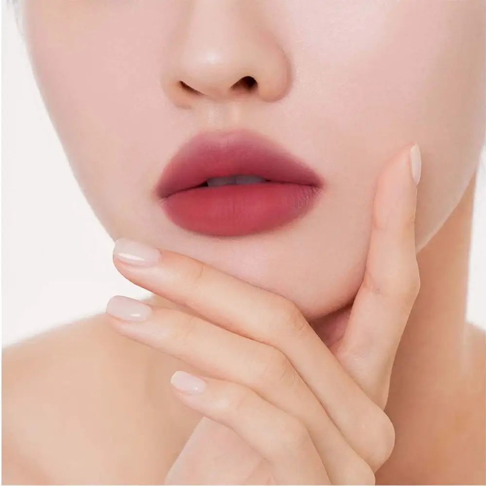 Close-up van lippen opgemaakt met een matte, roze lippenstift. Een hand raakt de wang aan.