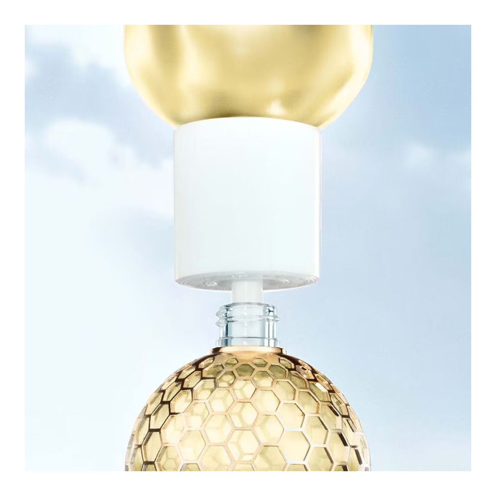 Gouden dop en witte sluiting. Glazen fles met gouden honingraatpatroon. Heldere vloeistof zichtbaar.