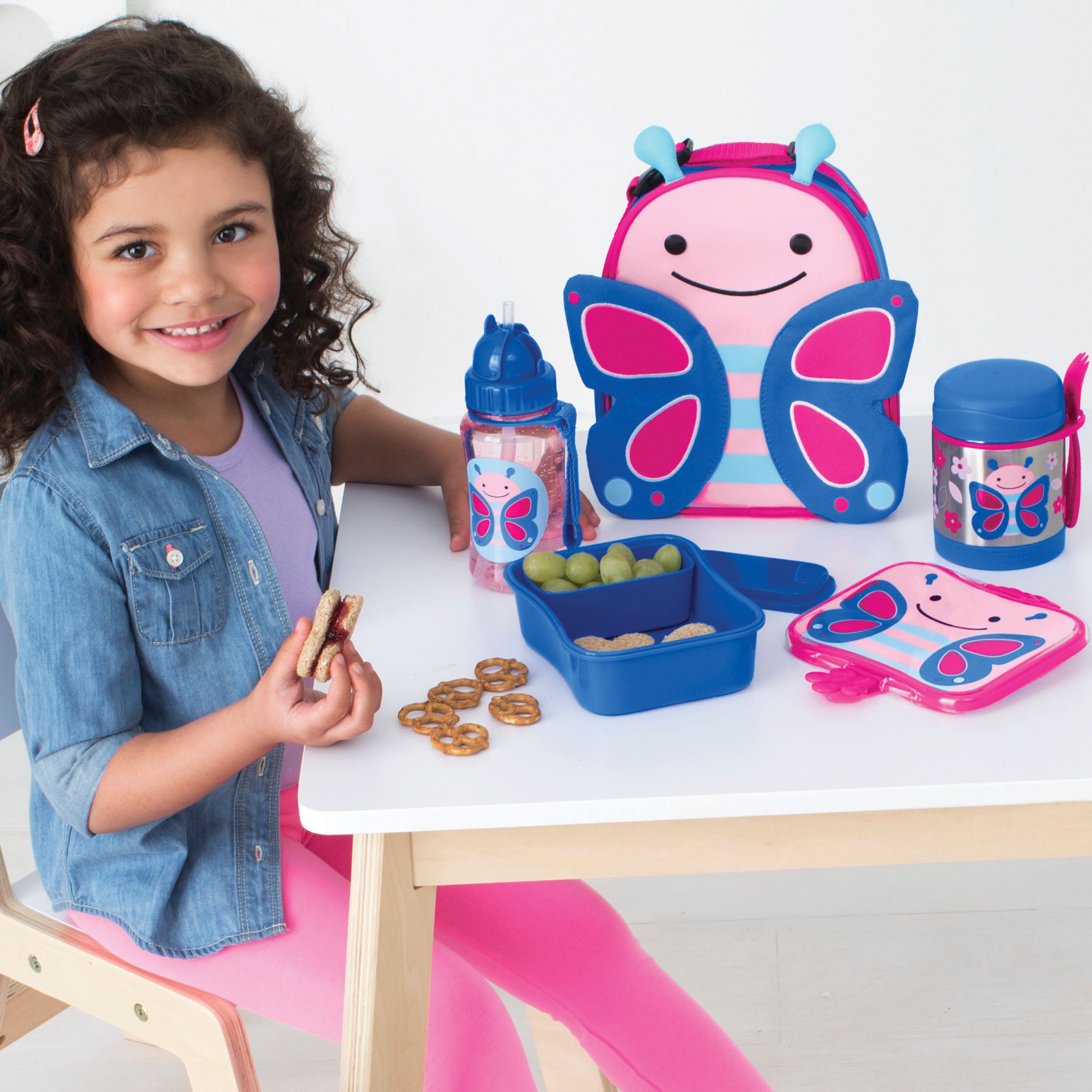 Kind met Skip Hop Zoo Papillon set. Rugzak, drinkfles, lunchbox, thermos. Roze, blauw, vlinderdesign.