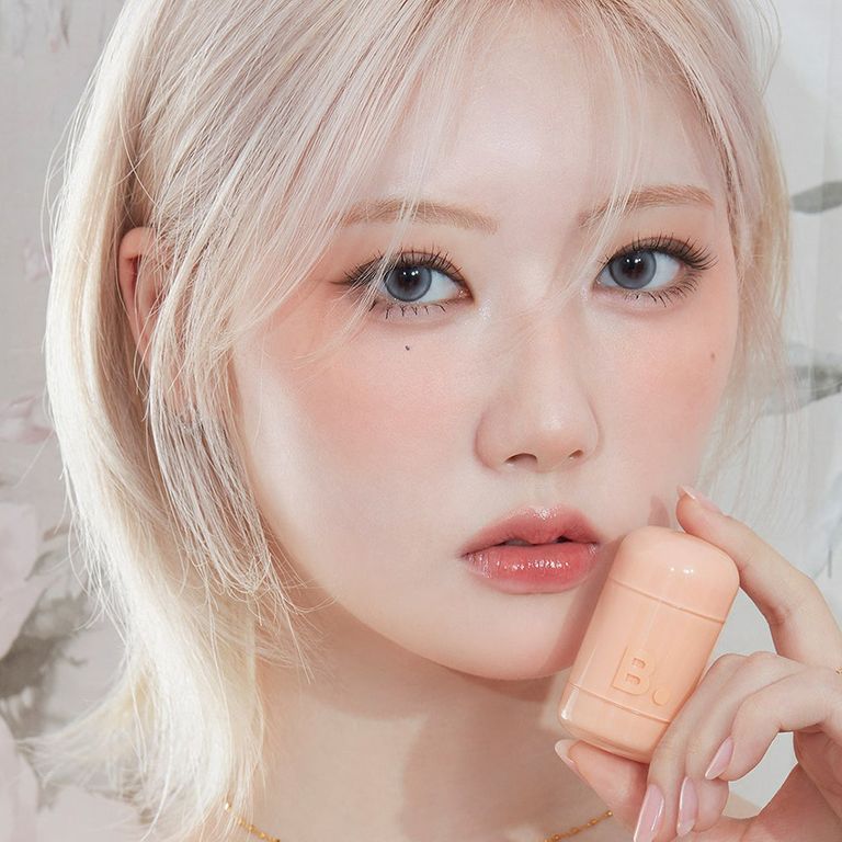 Une femme tient un récipient rose pâle avec le logo 'B.'.