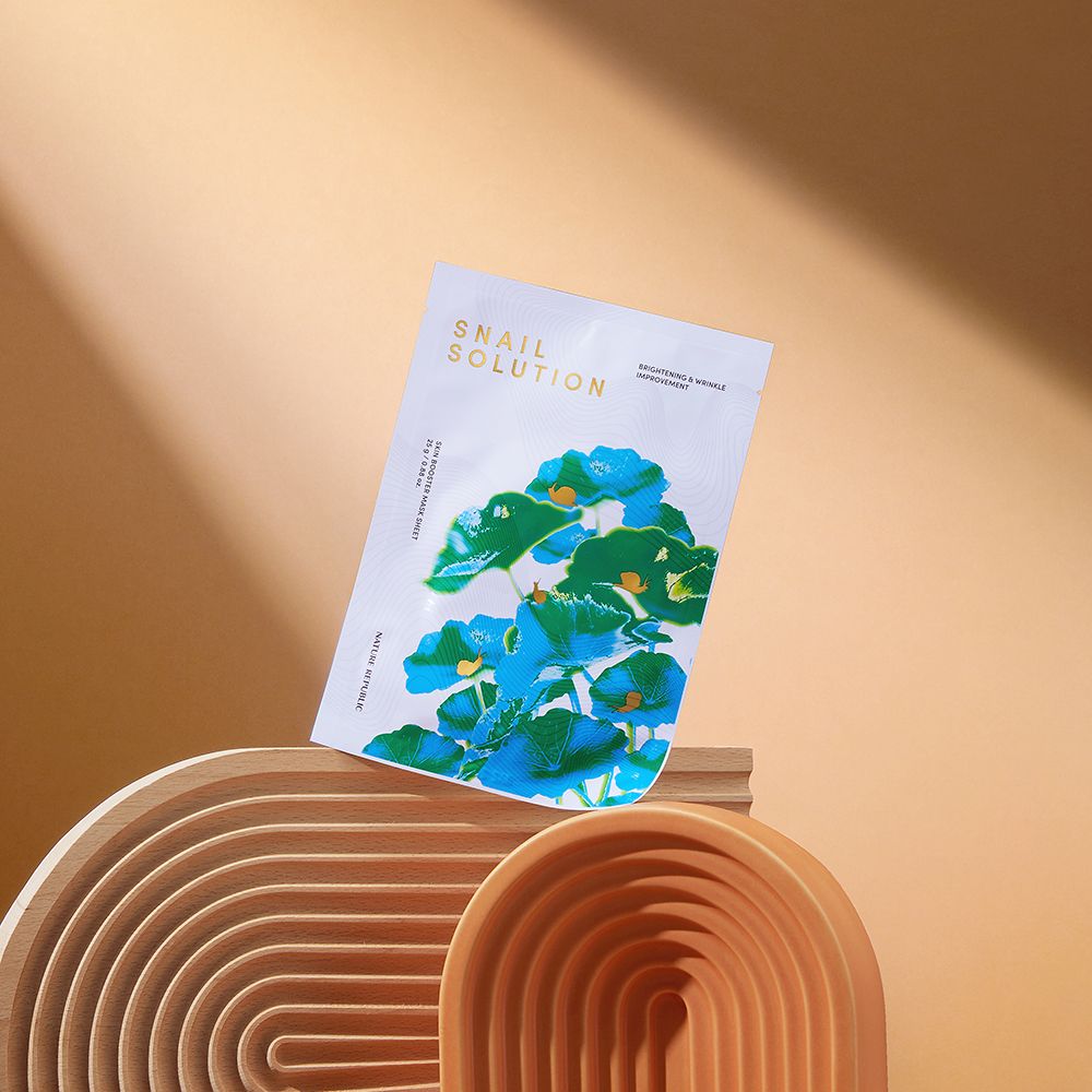 Gezichtsmasker op houten sokkel. Tekst: Snail Solution, Skin Booster Mask Sheet, Nature Republic. Bloemenmotief.