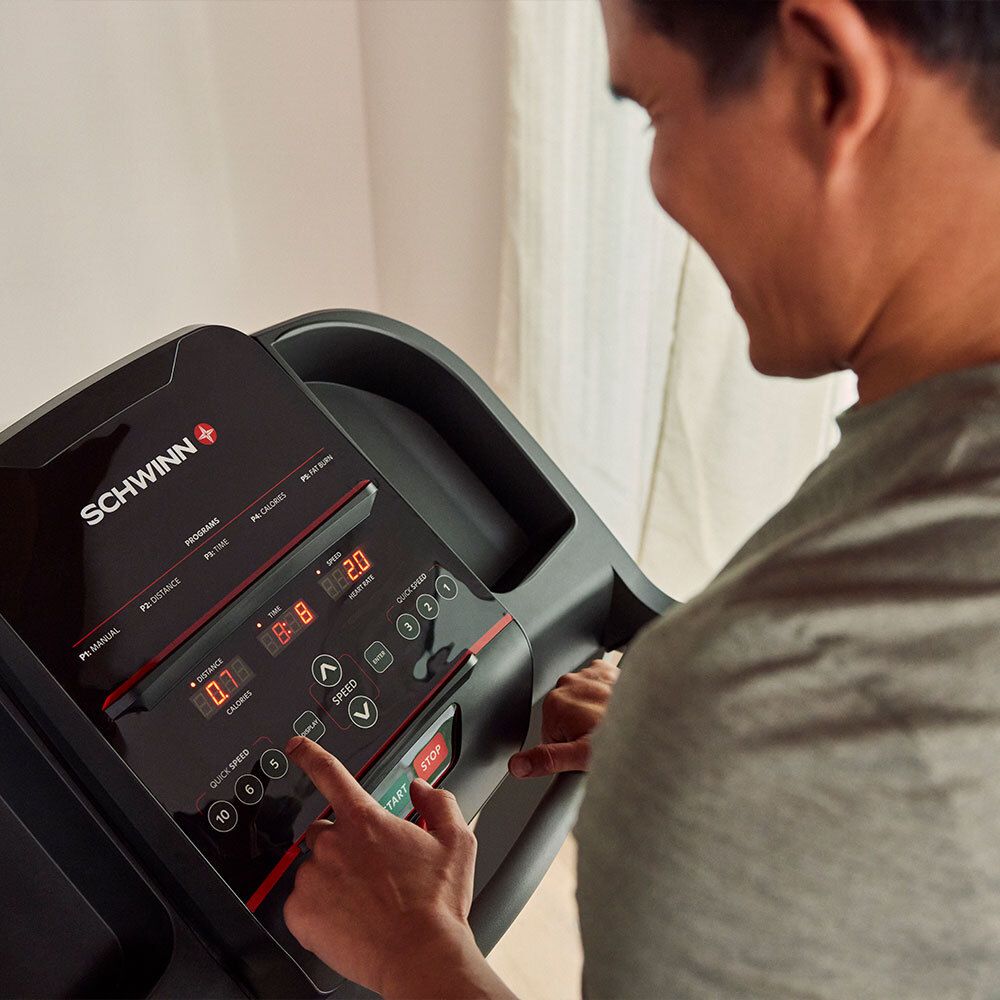 Personne utilisant la console d'un tapis roulant. Panneau noir avec écran et boutons. Logo Schwinn.