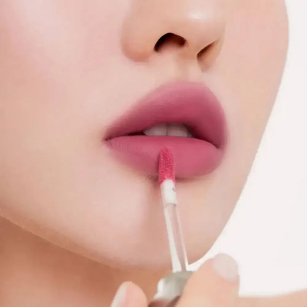 Close-up van lippen met roze lippenstift. Een applicator wordt gebruikt. Huidtint.