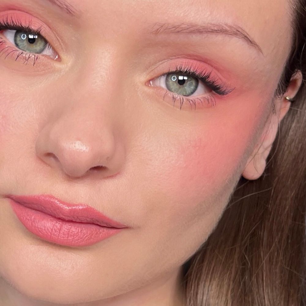 Gros plan d'un visage avec maquillage rose sur les yeux, les joues et les lèvres. Yeux verts.