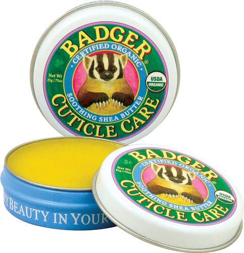Boîte ouverte avec baume jaune. Couvercle avec logo : blaireau, texte BADGER, Cuticle Care. Sceau USDA Organic. Boîte bleue.