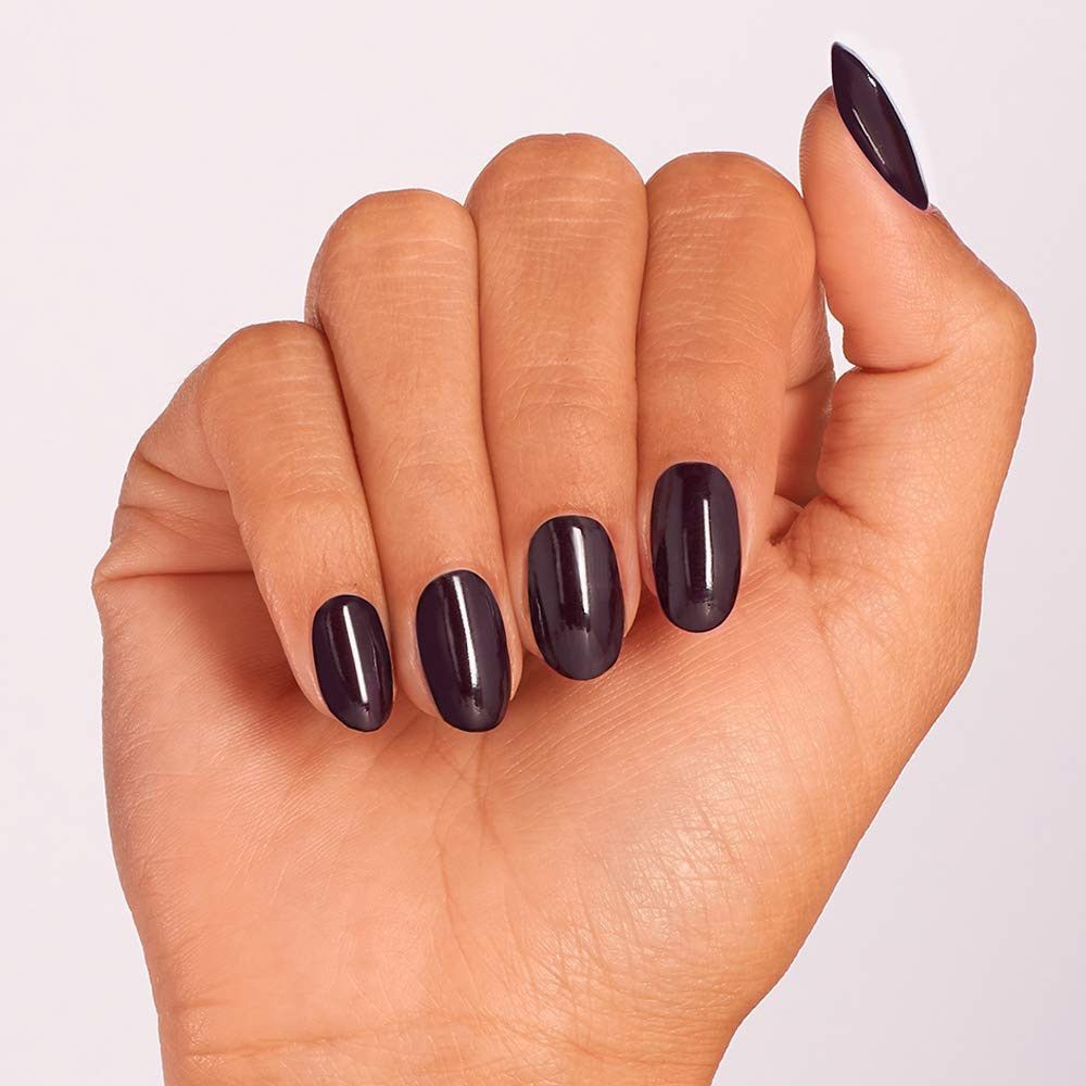 Main avec ongles vernis en violet foncé. Quatre ongles, forme ovale, brillants.