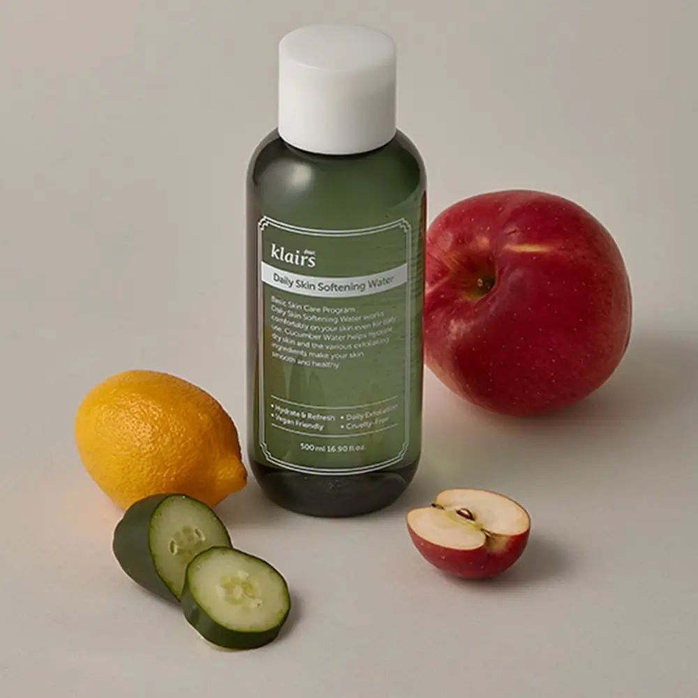 Flacon vert avec étiquette produit, à côté citron, pomme, tranches de concombre. Sur fond clair.