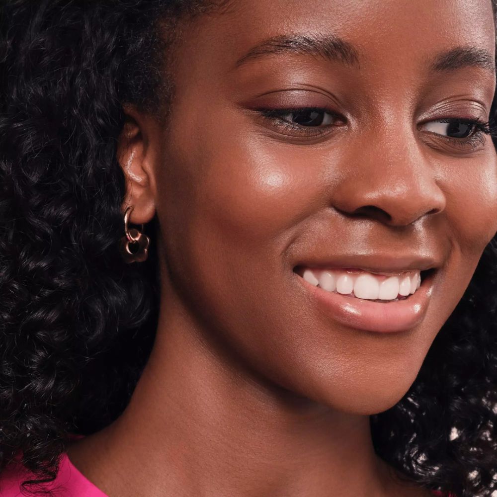 Gros plan d'une femme souriante. Boucles d'oreilles dorées. Lèvres roses.