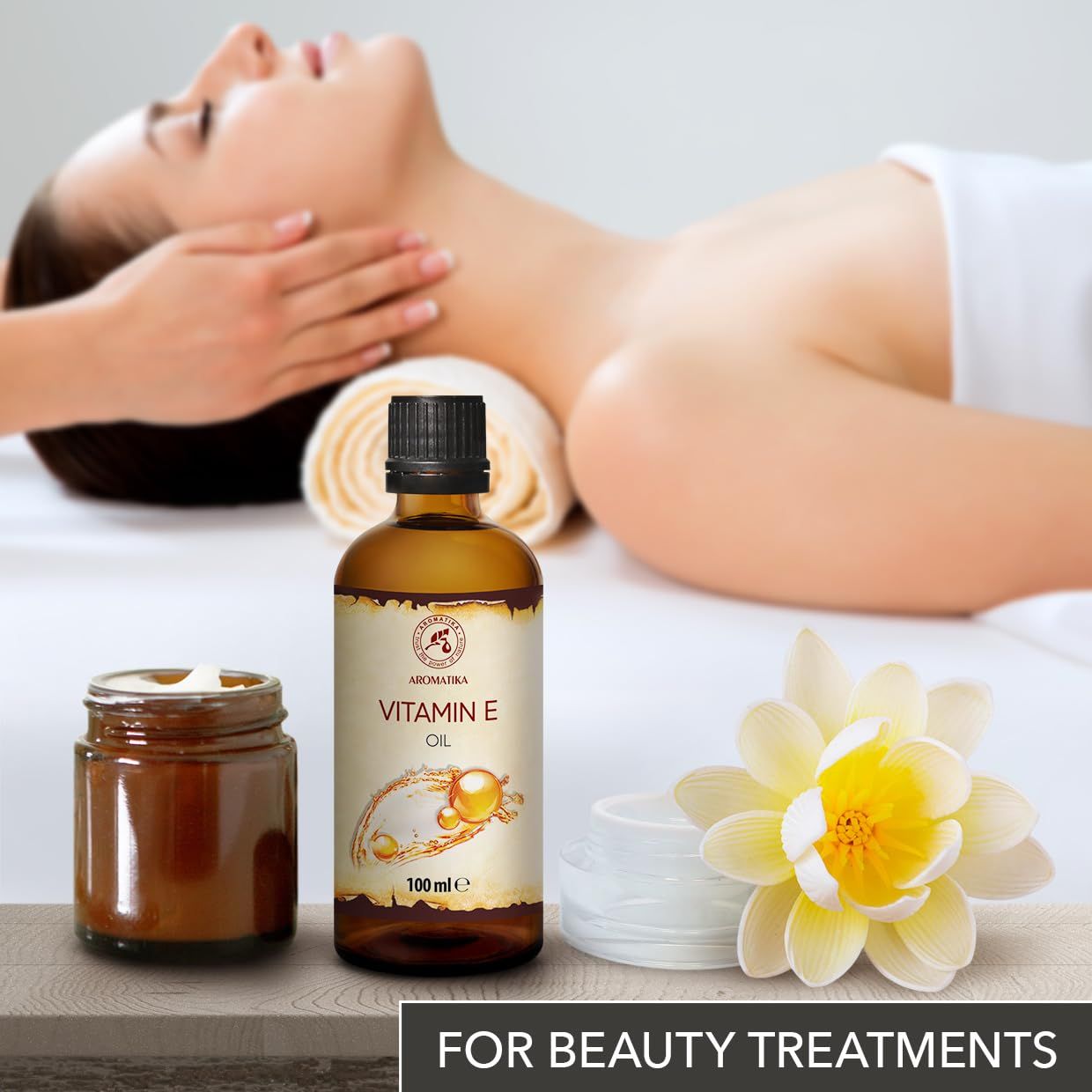 Wellness-scène met liggende vrouw, AROMATIKA Vitamine E Olie fles, potje en bloem. Tekst "For Beauty Treatments".