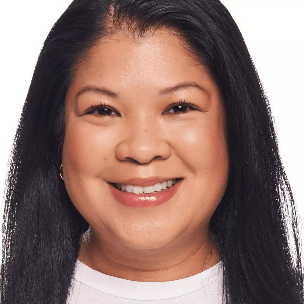 Portrait d'une femme avec une peau lisse. Elle porte du fond de teint. Cheveux noirs, souriante.