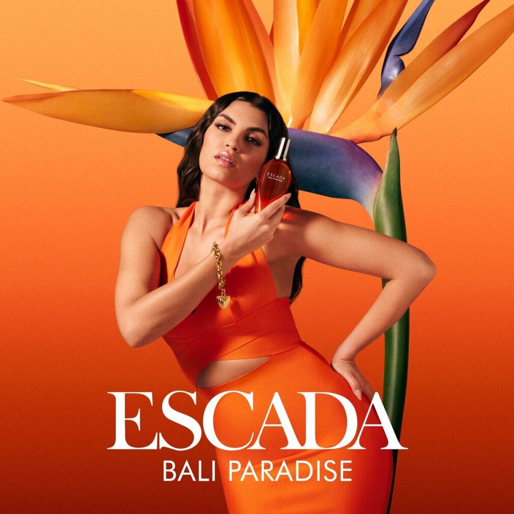 Femme tenant Escada Bali Paradise EdT Nat. Spray. Femme en orange, produit en main.