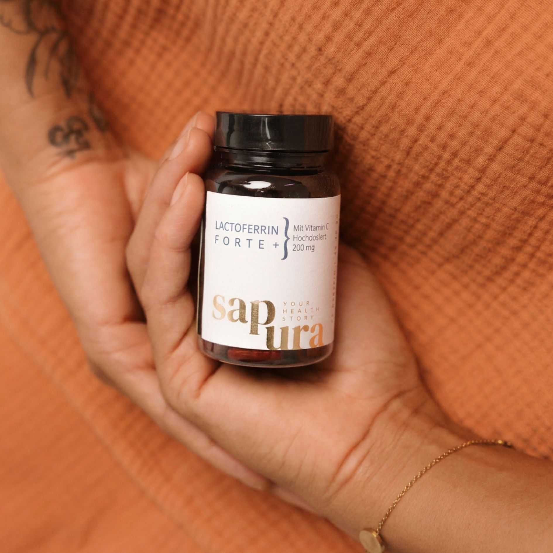 Mains tenant une bouteille de Lactoferrin Forte. Sapura Health.