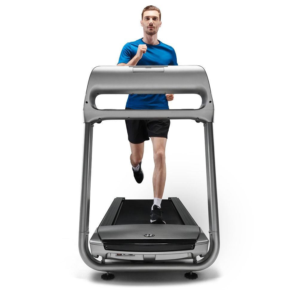 Tapis de course gris avec coureur. Éléments visibles : mains courantes, console, surface de course. L'homme porte des vêtements de sport.