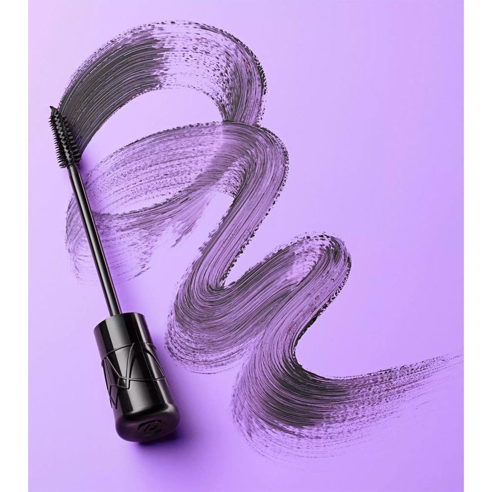 Applicateur de mascara et trait de mascara noir sur fond violet. Forme ondulée.