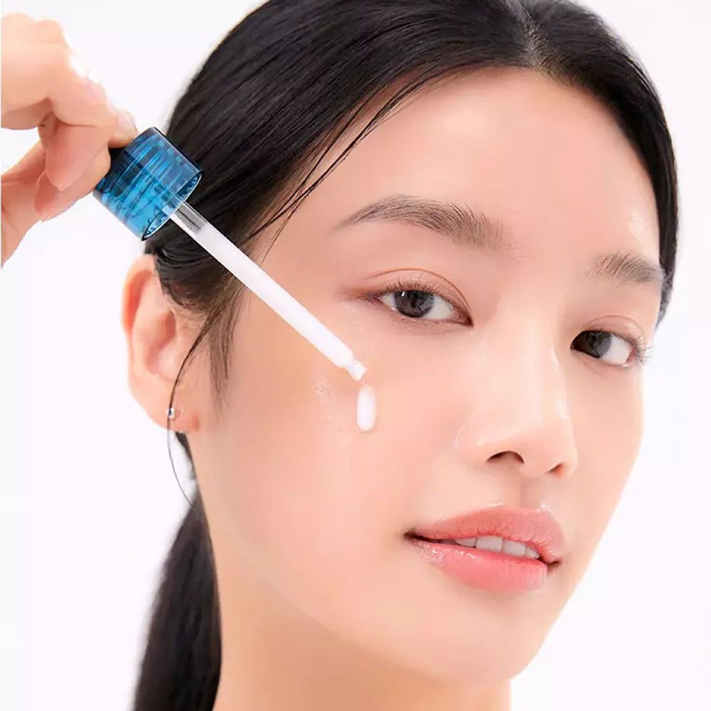 Een vrouw die serum op haar gezicht aanbrengt met een pipet. Het product is niet benoemd.