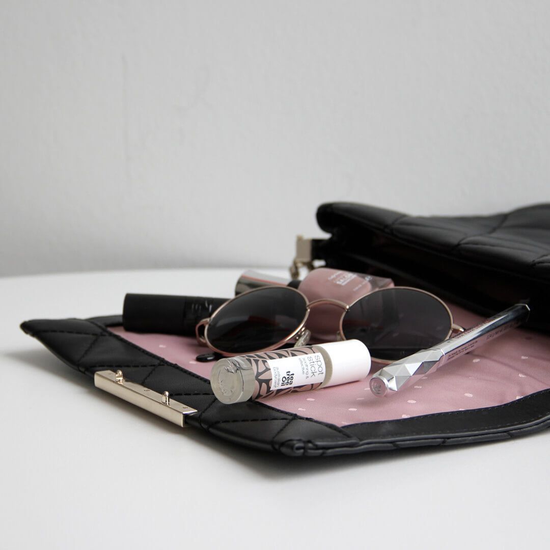 Spot stick en accessoires in handtas. Zonnebril, lippenstift, etc. Zwarte tas.