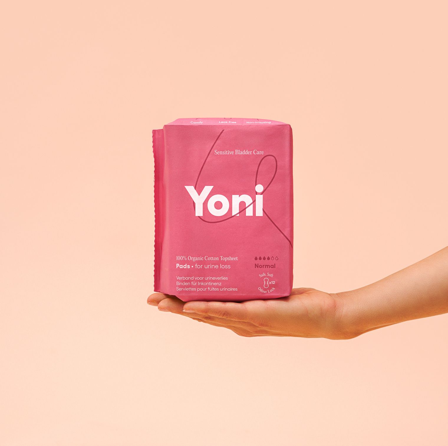 Emballage rose avec produit. Inscription 'Yoni'. '100% Organic Cotton Topheet Pads for urine loss'. Tenu par une main.