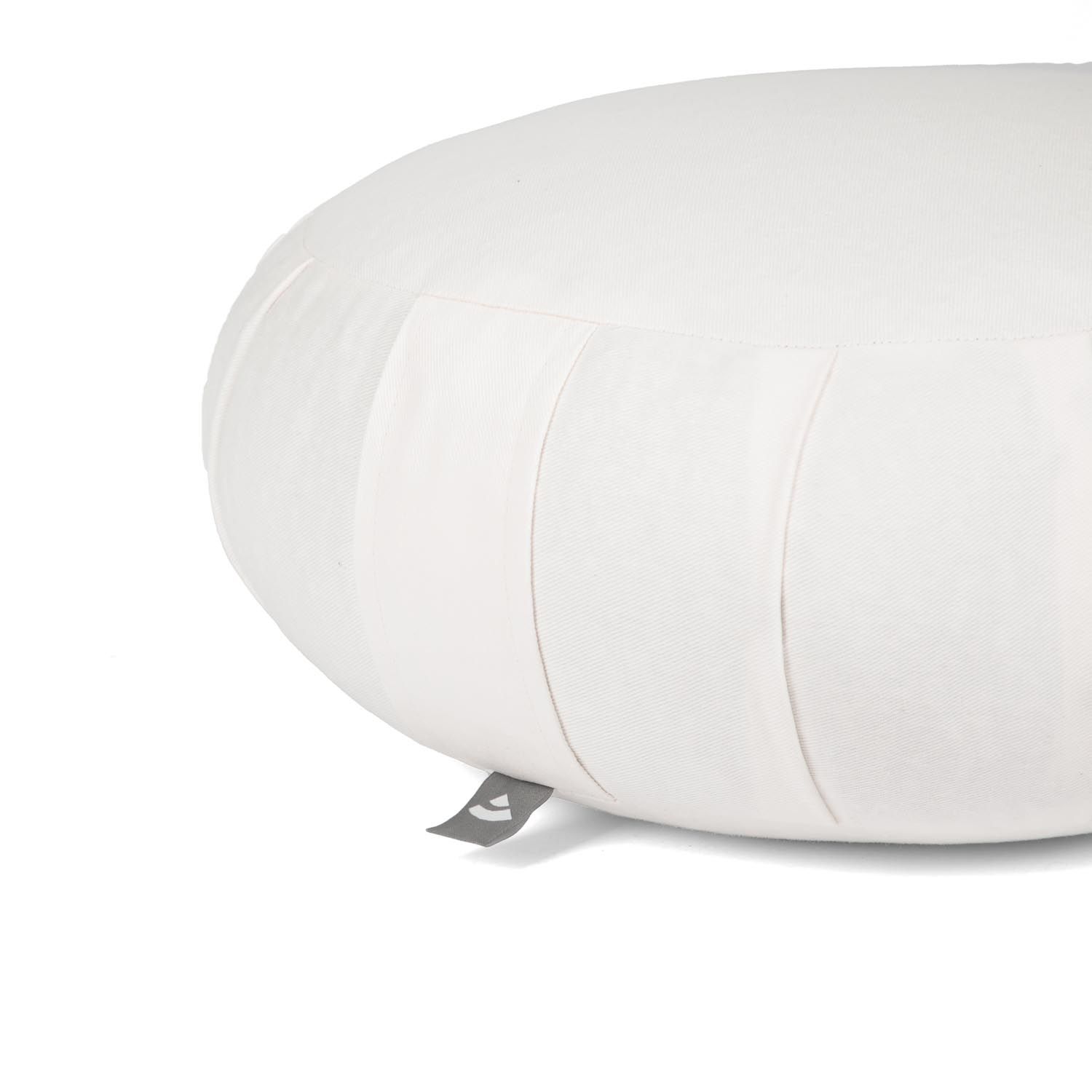 Gros plan d'un coussin de méditation blanc, rond, avec plis et étiquette.