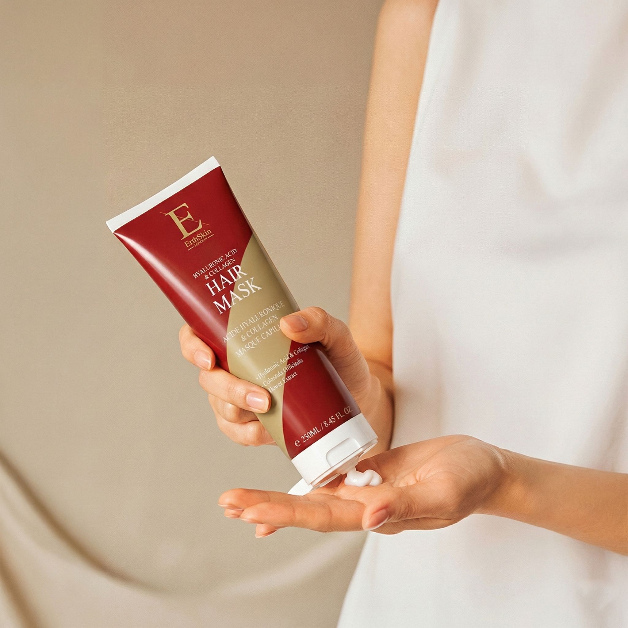 Une main tient un tube rouge de masque capillaire à l'acide hyaluronique et au collagène. De la crème est pressée.