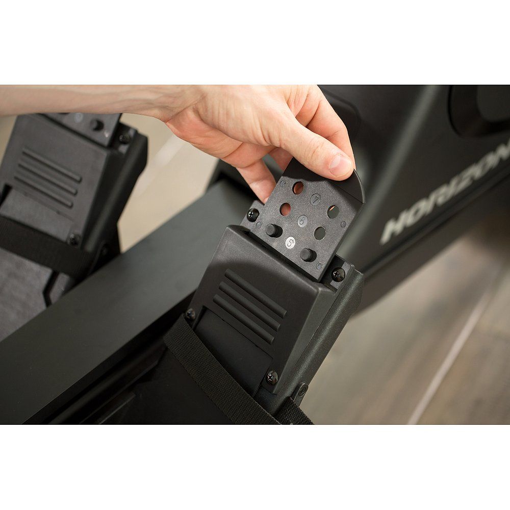 Close-up van onderdelen van de roeimachine. Zwarte plastic onderdelen met schroeven en gaten. Hand houdt onderdeel vast.