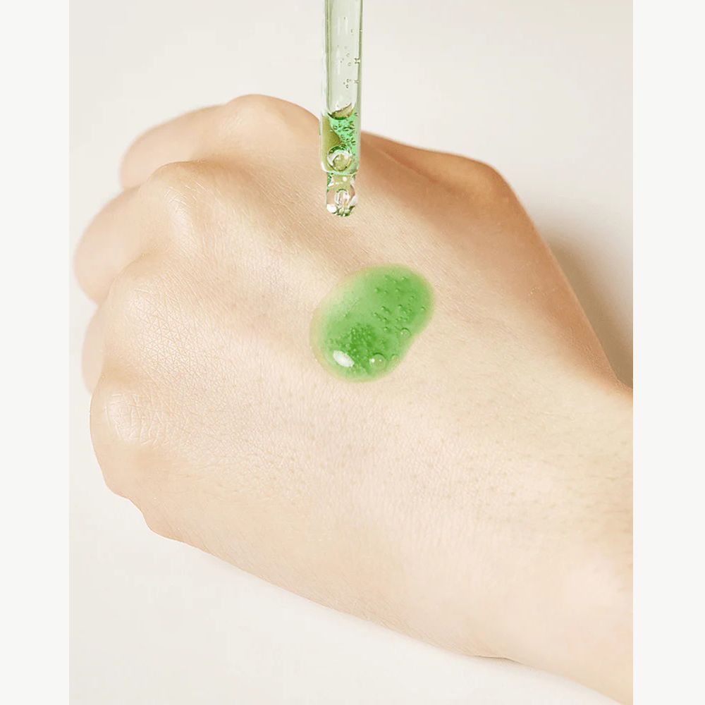 Main avec goutte de sérum vert. Sérum sur la peau. Pipette au-dessus.