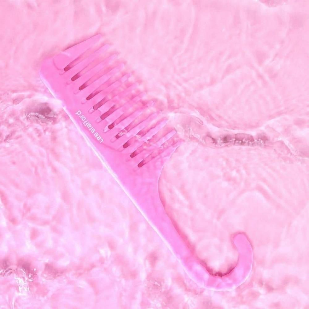 Een roze kam met brede tanden drijft in licht golvend water.