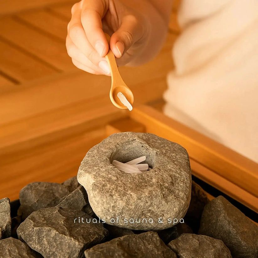 Hand houdt houten lepel met kristallen boven steen met kristallen. Opschrift: rituals of sauna & spa.