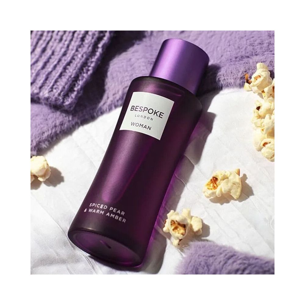 Flacon violet avec bouchon. Inscription: Bespoke London, Woman, Spiced Pear & Warm Amber. Entouré de pop-corn.