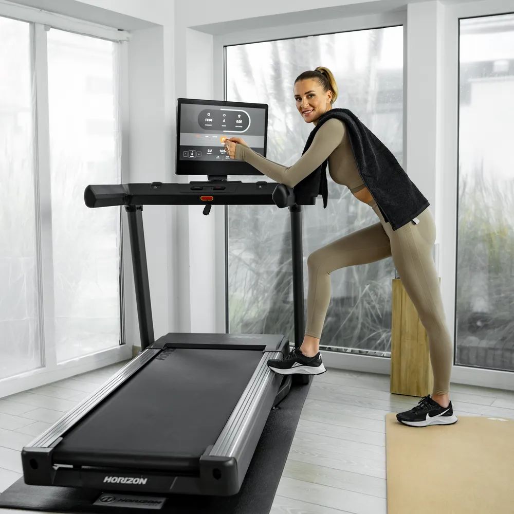 Femme appuyée sur un tapis roulant. Tapis roulant noir avec écran. Logo Horizon visible.