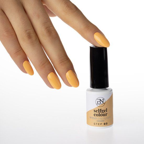 Main avec ongles oranges à côté d'un flacon de vernis à ongles. Flacon avec bouchon noir, étiquette blanche avec logo et nom du produit.